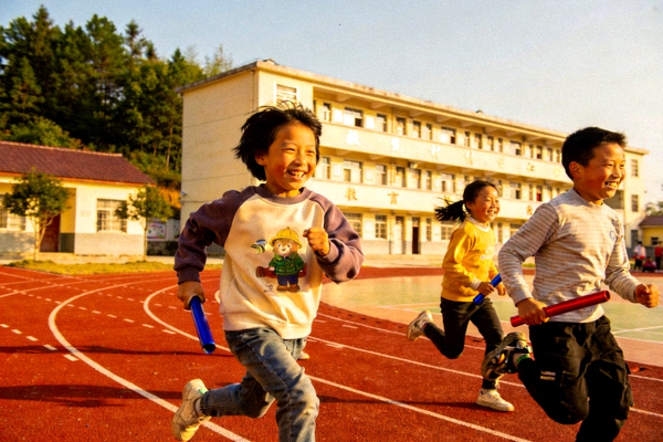 乡村小学体育课上，孩子们在新建的塑胶跑道上快乐地进行接力跑比赛