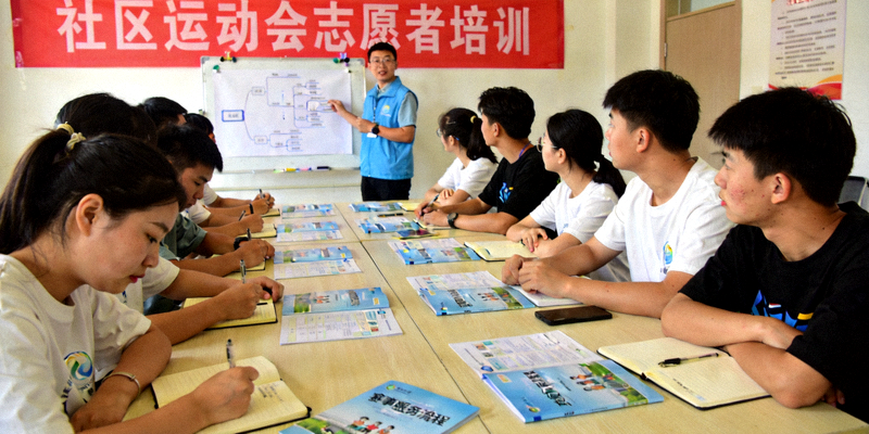 社区运动会志愿者培训现场，年轻志愿者认真学习赛事服务流程