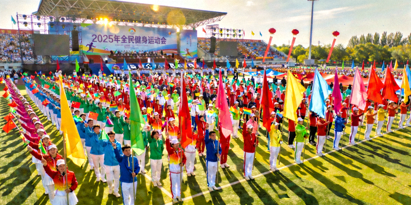 2025年全民健身运动会开幕式盛况，数千名参与者组成彩色方阵，挥舞旗帜，气氛热烈